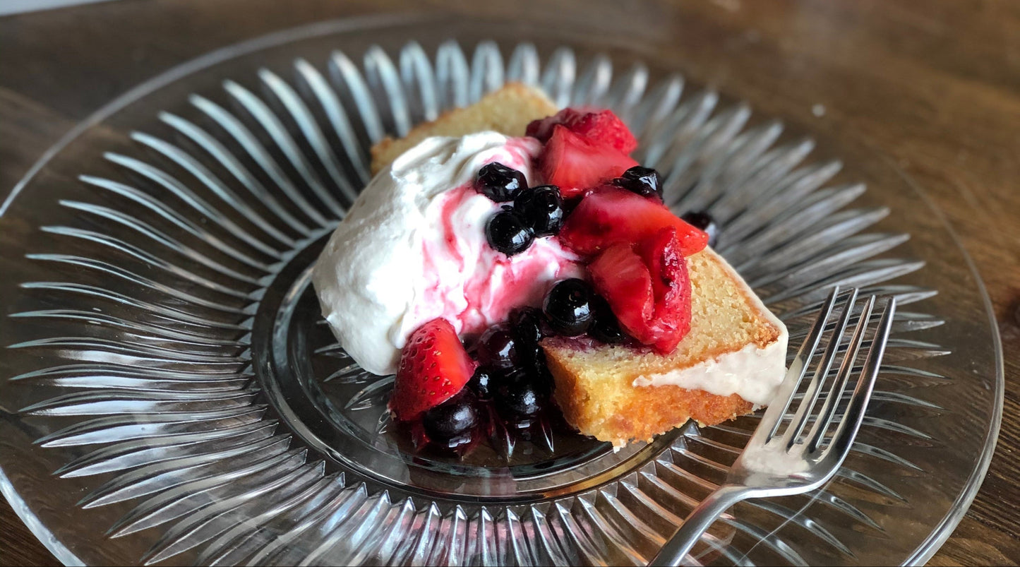 Slice of cake with berries on a glass plate with a fork, on a wooden table.