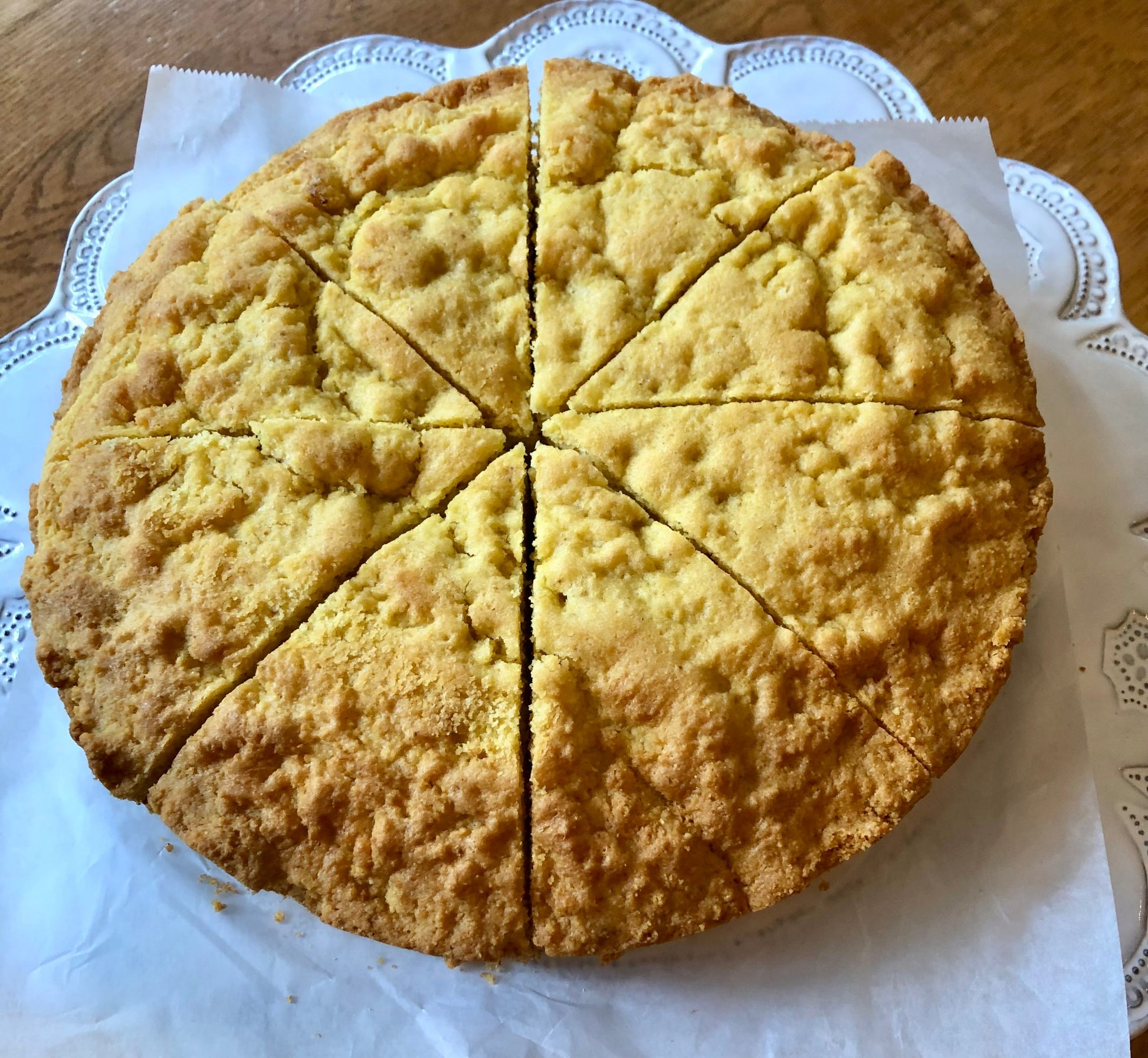 Round baked cornbread cut into slices on a white paper doily.