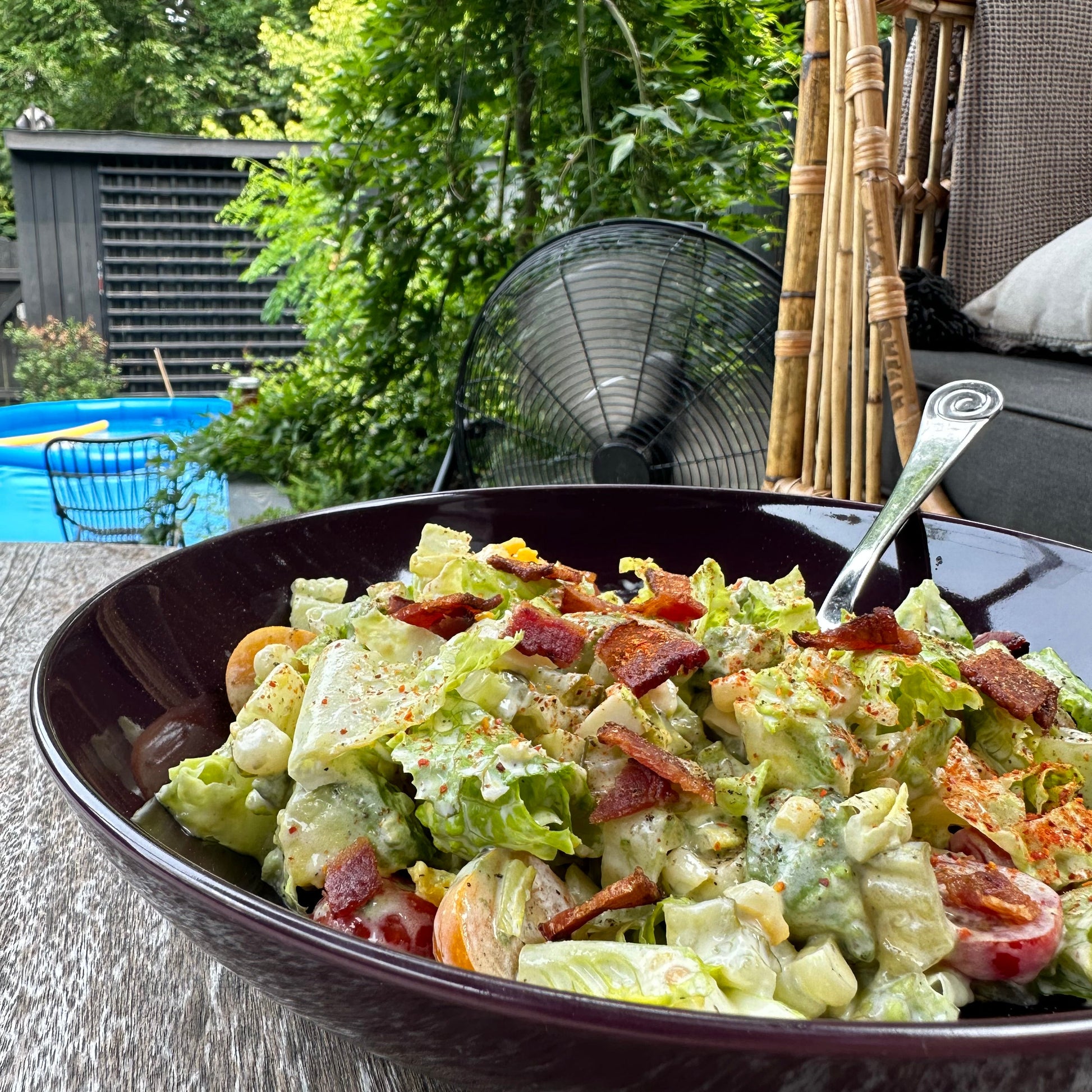 Salad with bacon in a bowl on a wooden table outdoors