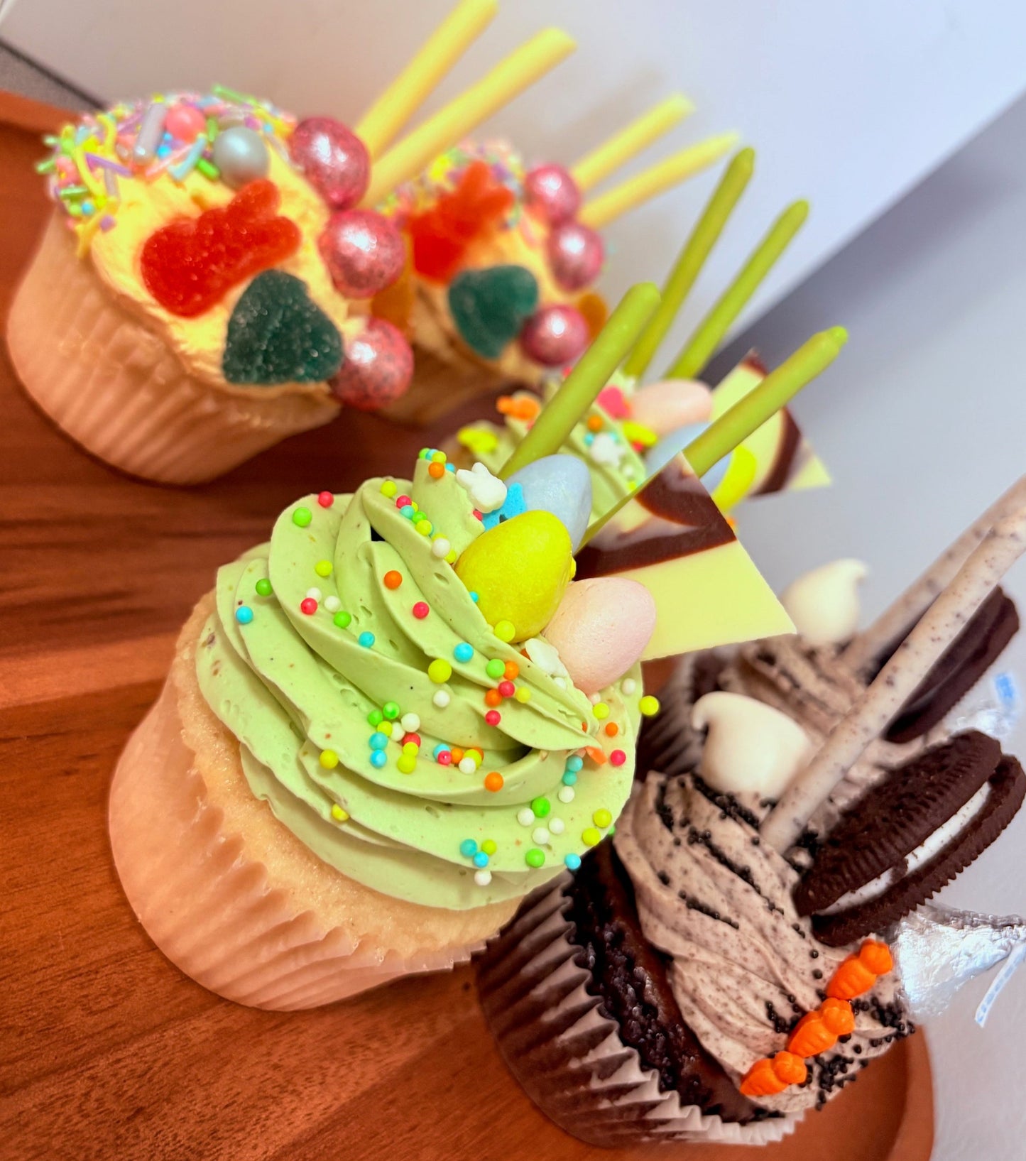 Six decorated cupcakes on a wooden surface with a white background